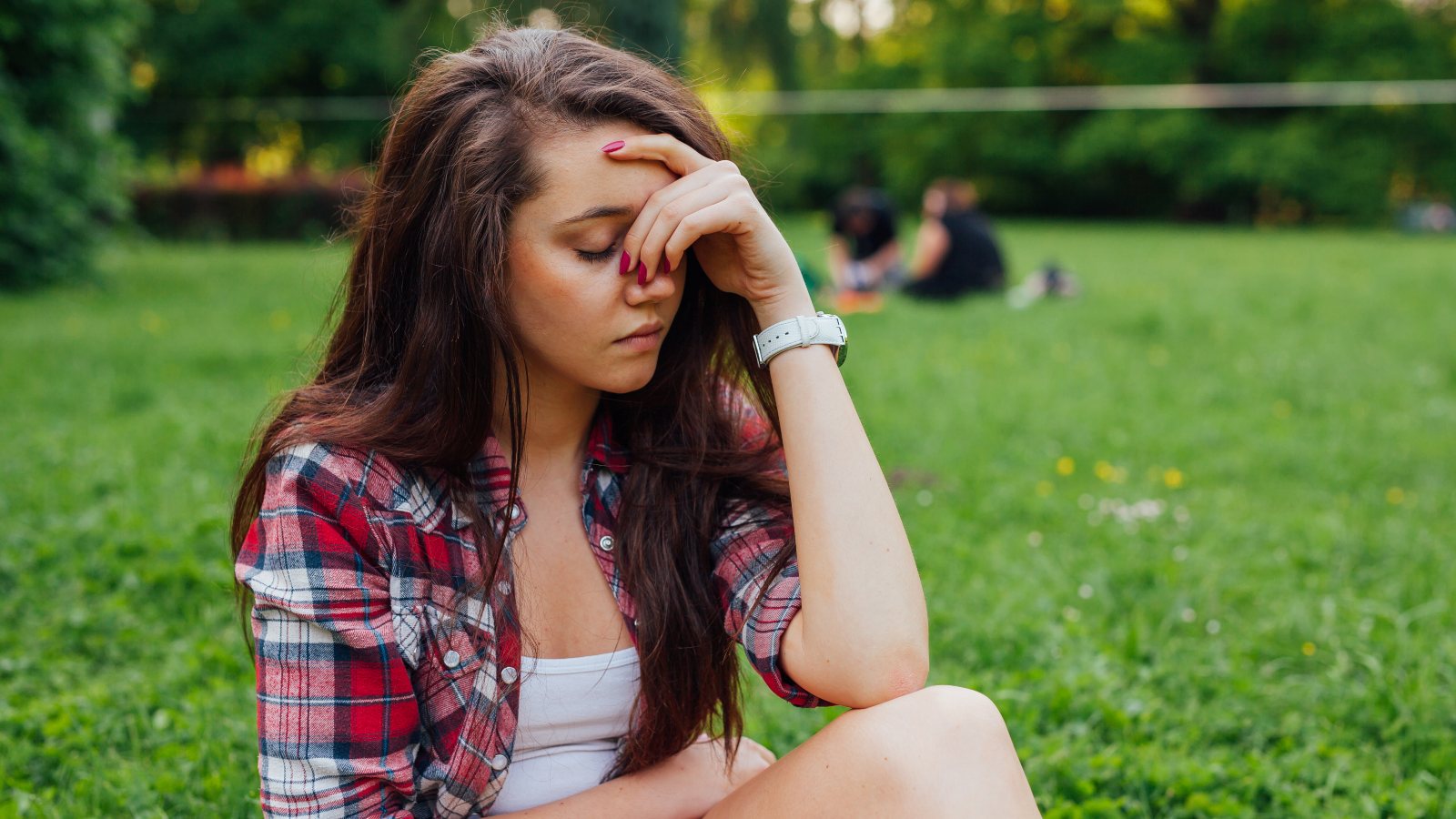 Girl sitting in the park on the grass. She has headache. woman